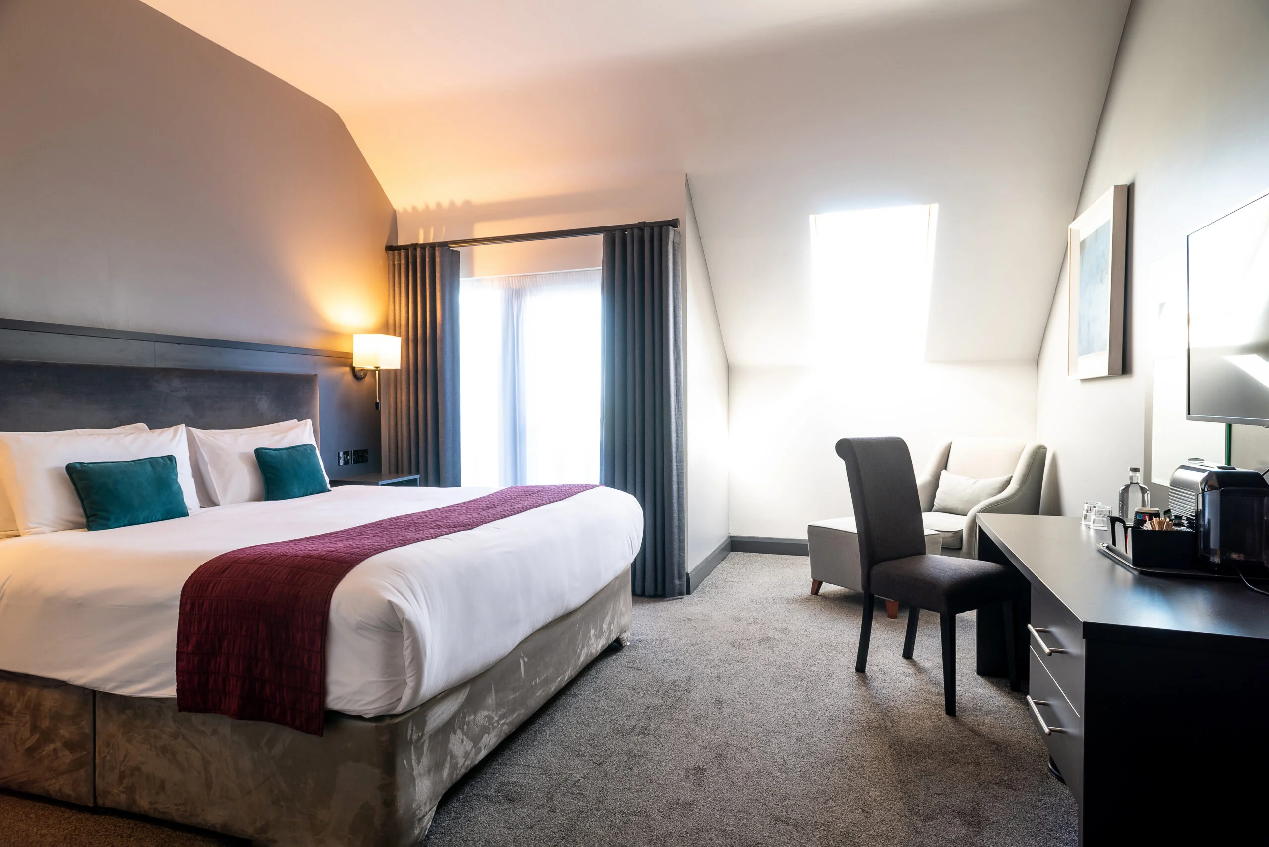 The Cliffs of Moher Hotel in Liscannor. Image of a double bedroom in the hotel with two queen sized beds with red blankets overlaying white duvets.
